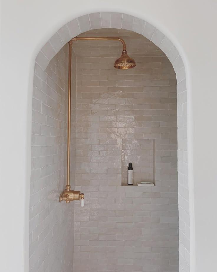 A sleek shower design with a brass shower head and a bright white wall.