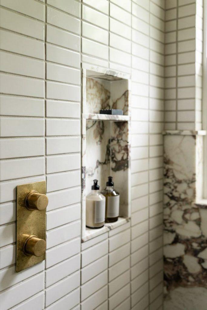 Modern bathroom design with a sleek marble wall and a contemporary brass shower.