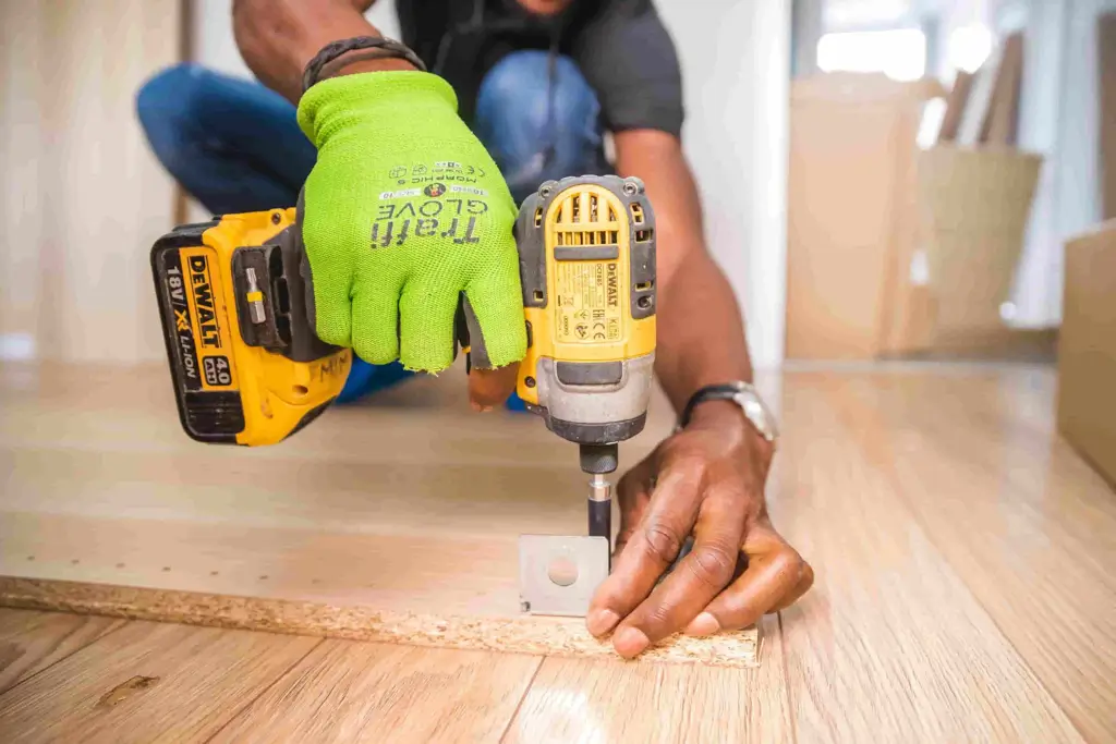 A man is drilling into wood, working on a DIY project in a well-lit area.