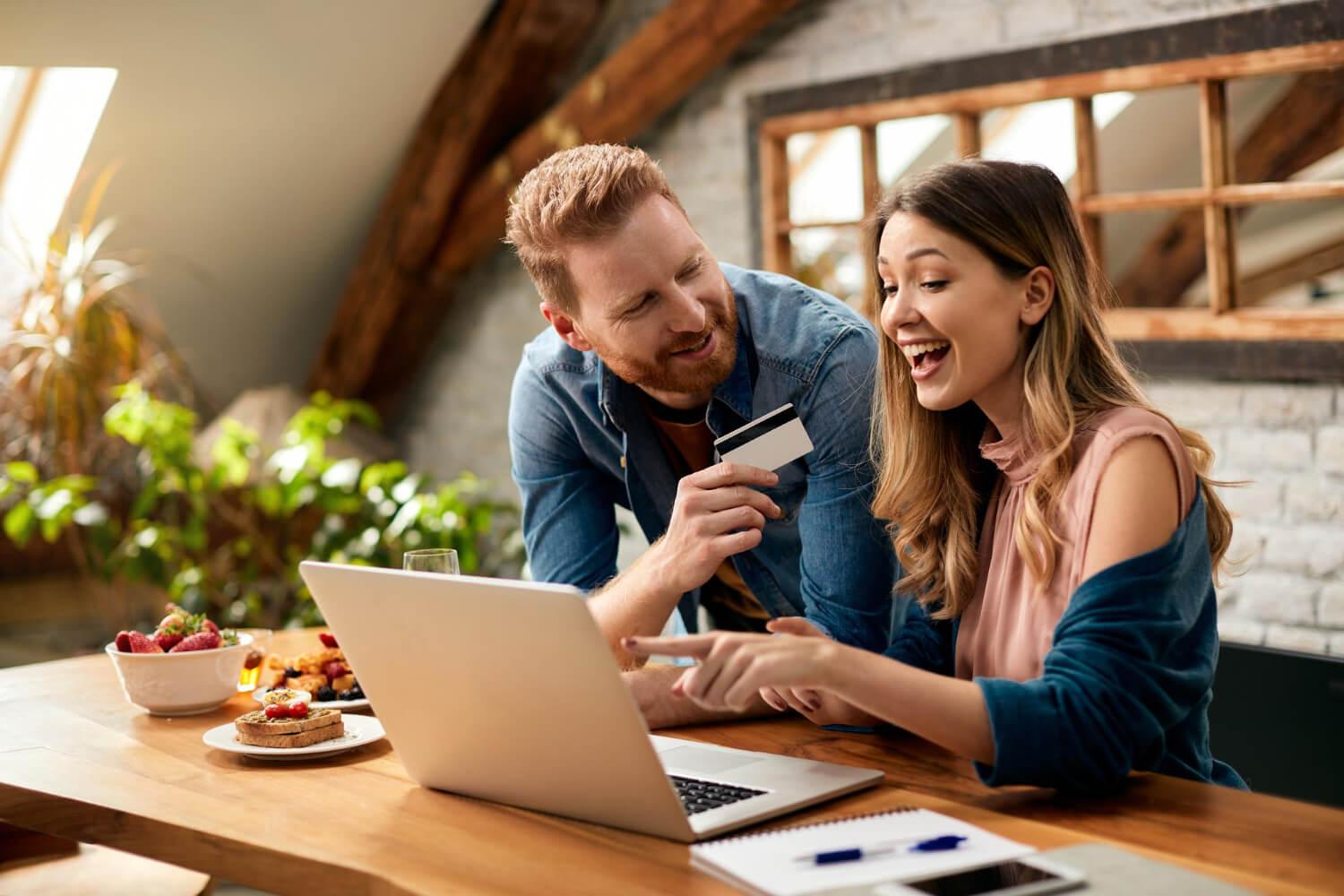 Couple shopping online, using a credit card to complete their purchase on a laptop.