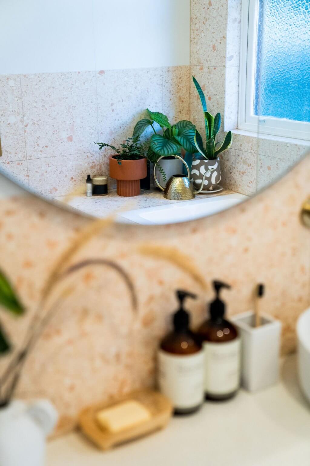 Brass tapware close-up against peachy pink terrazzo tile with styled toiletries on ledge