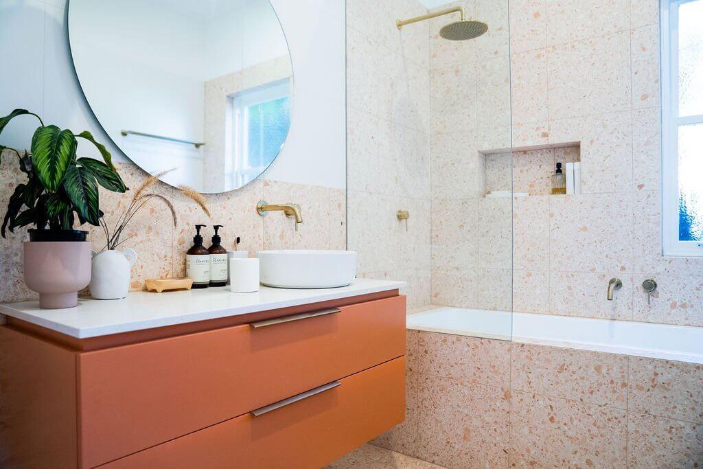 Round mirror with brass tapware above terracotta vanity and terrazzo tiled wall