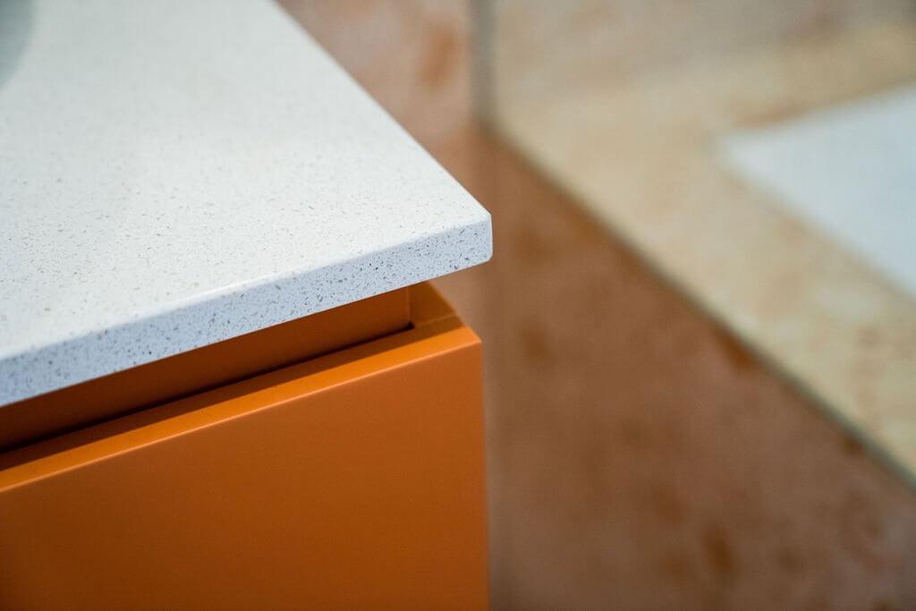 Close-up of white stone countertop edge on bold terracotta vanity cabinet