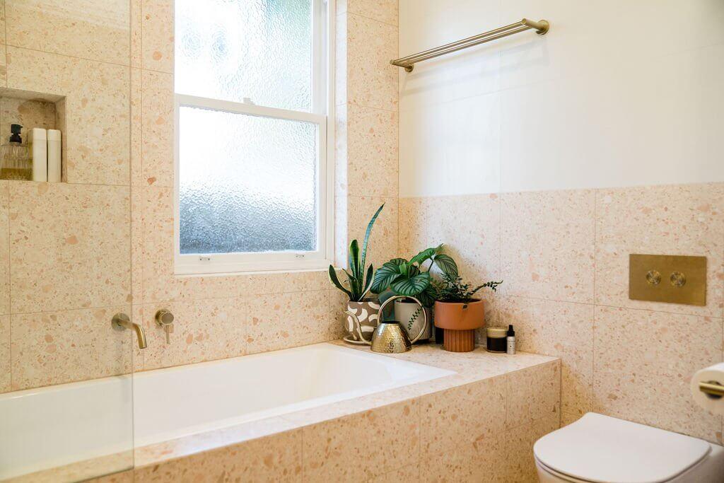 Frosted window above terrazzo tiled bathtub with potted plants on the ledge