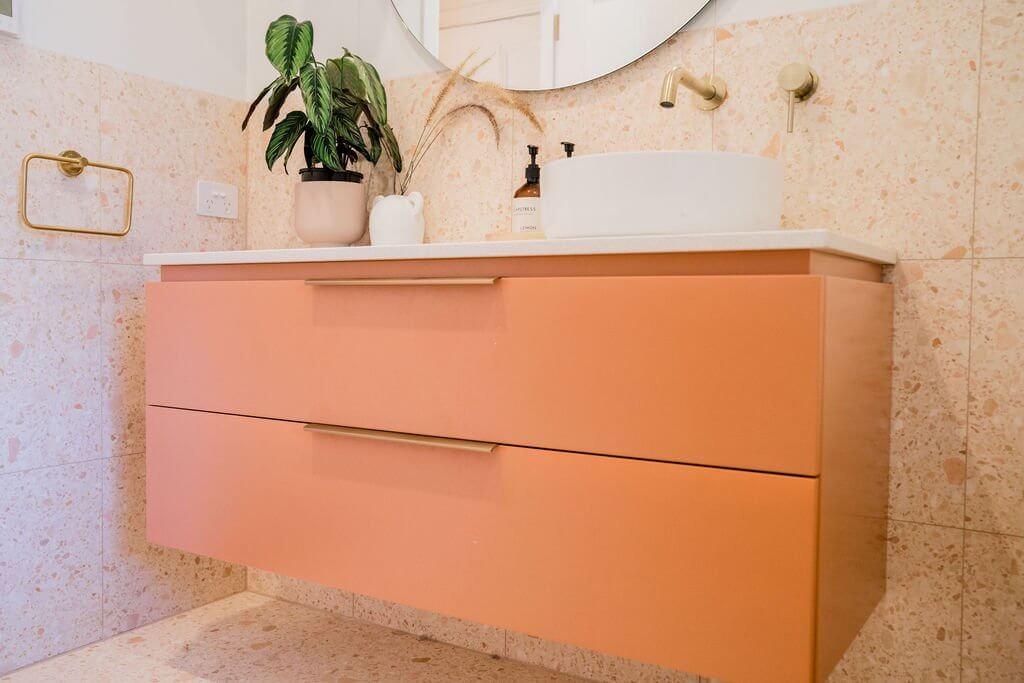 Close-up of bold terracotta vanity cabinetry with round mirror and potted plant