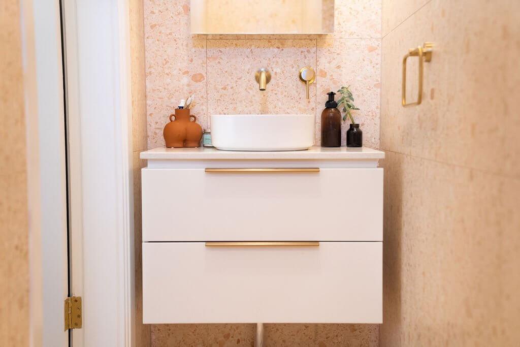 Close-up of white vanity with round mirror against peachy pink terrazzo tiled wall