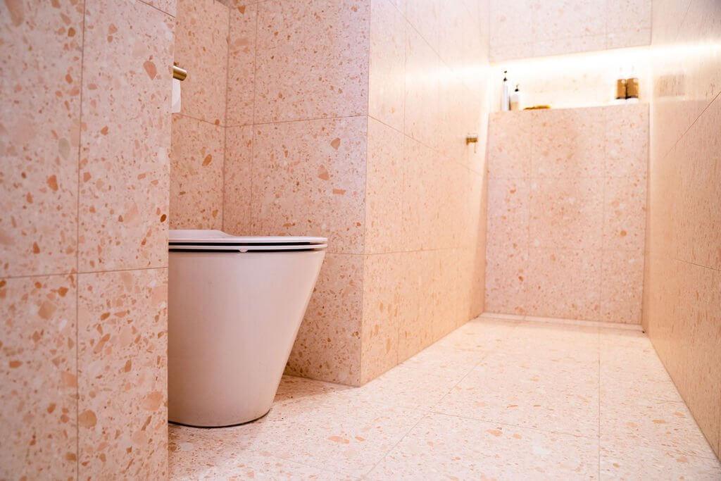 White toilet against peachy pink terrazzo tiled wall
