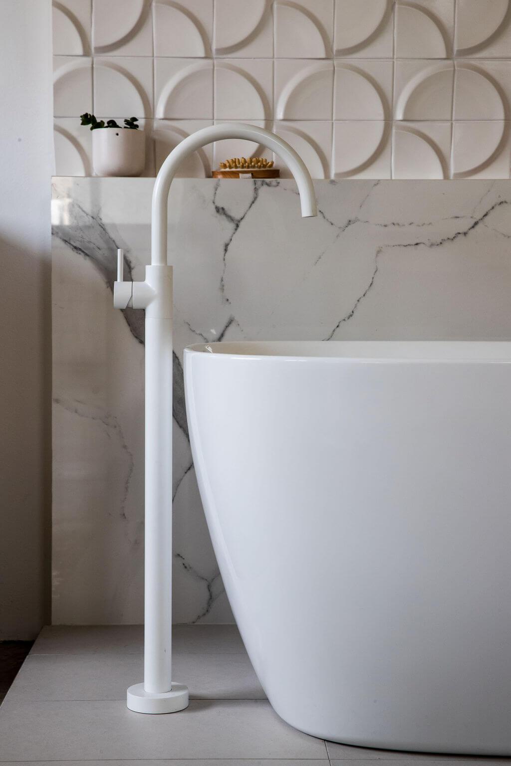 A pristine white bathtub and faucet complemented by a marble wall backdrop.