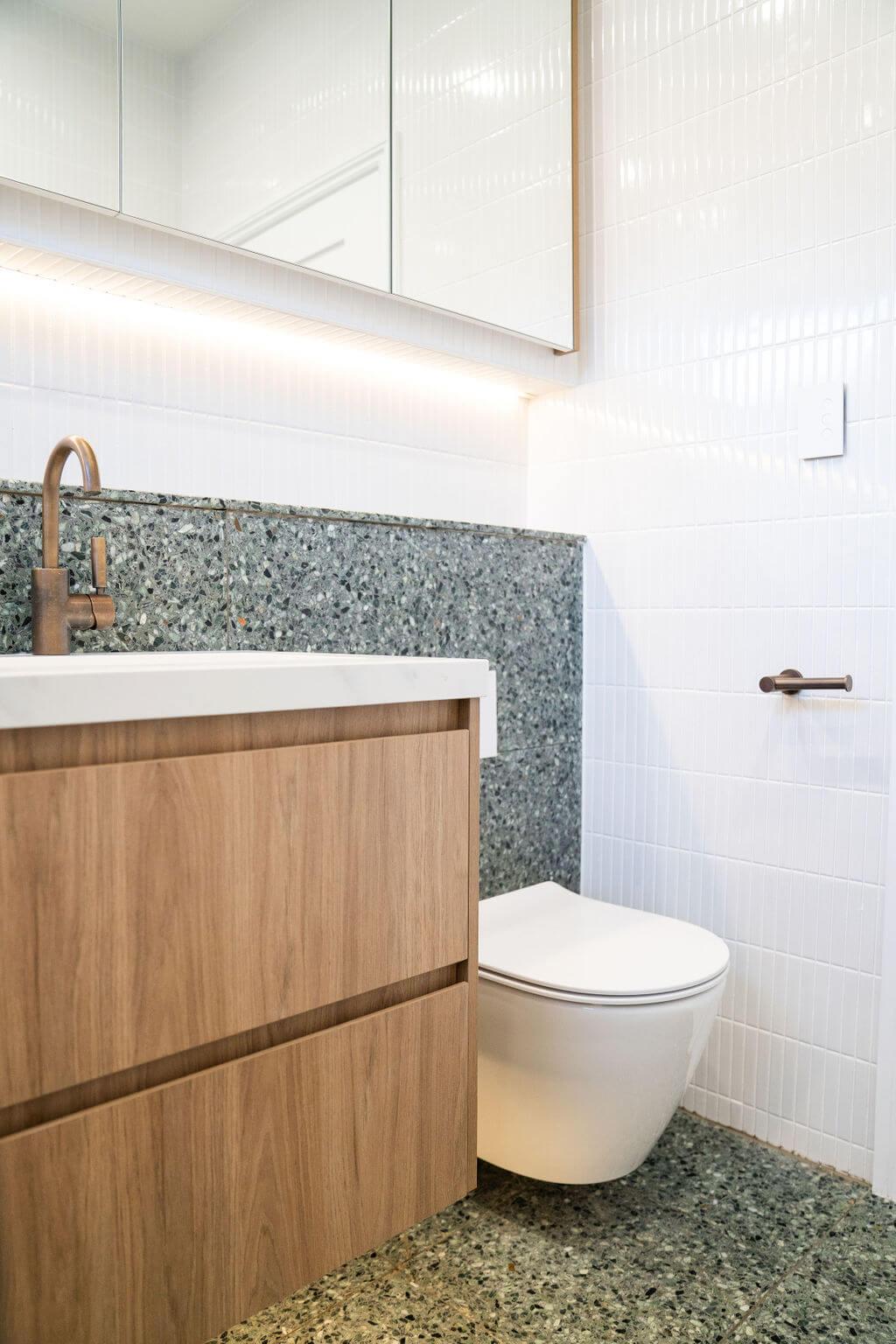 A bathroom featuring a wooden vanity and a white toilet, with neutral-colored walls and tiled flooring.