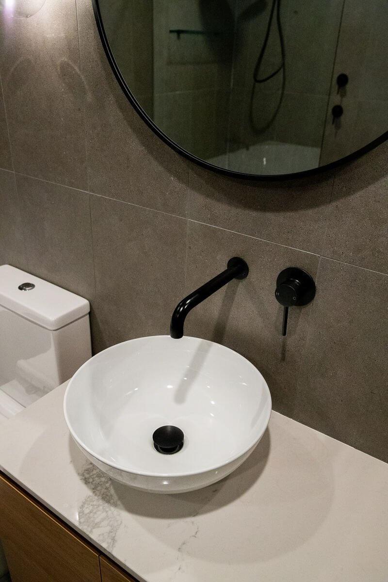 Round mirror, matte black wall-mounted tap and vessel sink on timber vanity with marbled top