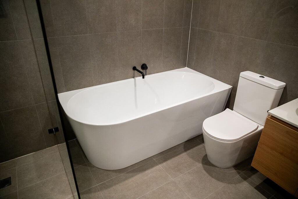 Freestanding bathtub with matte black wall-mounted tapware and dark grey tiled wall
