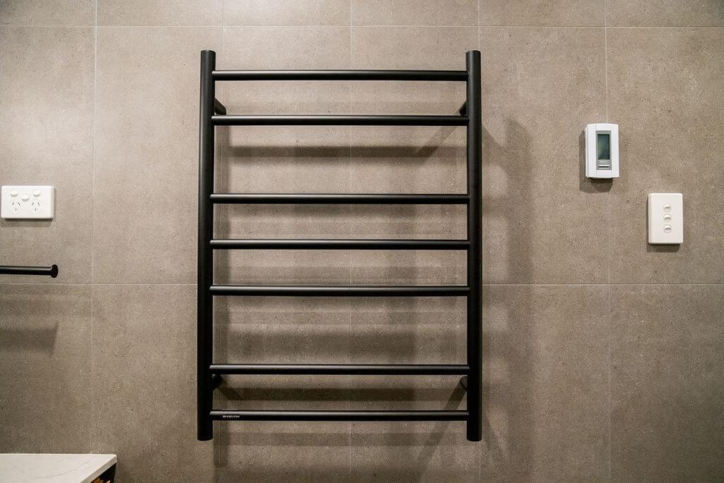 Matte black heated towel rail against dark grey porcelain tile wall