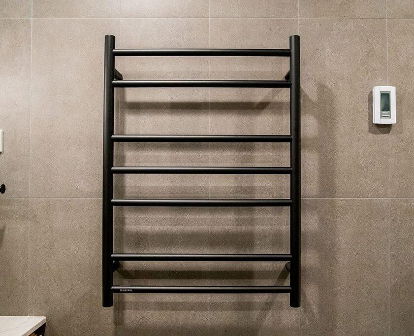 A sleek black heated towel rack mounted on a bathroom wall, providing warmth and convenience for towels.