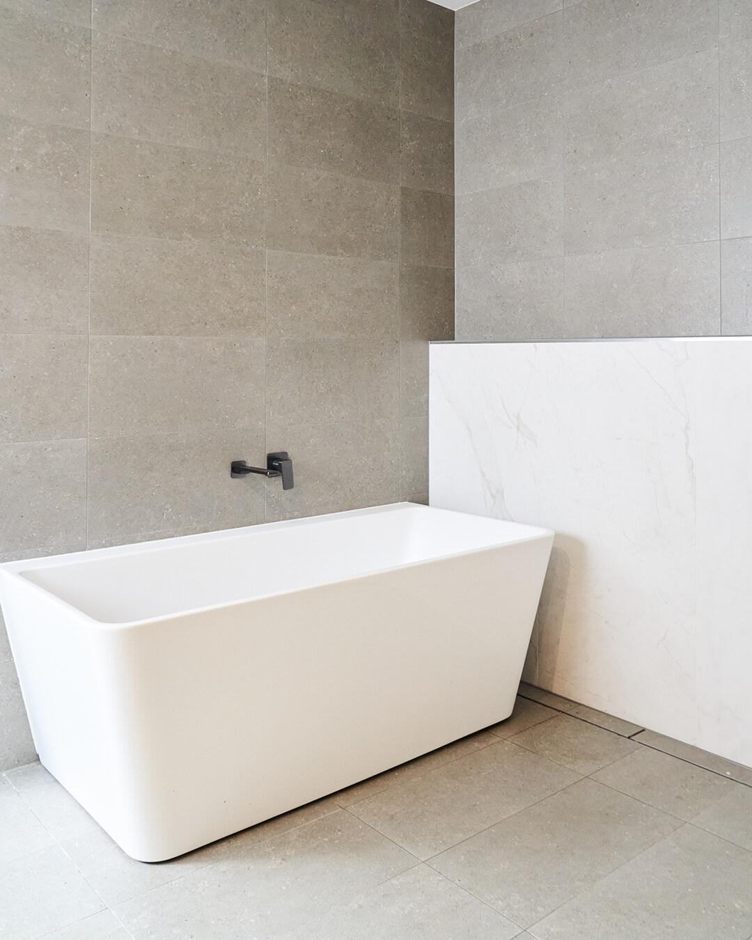 A white bathtub is centrally located in a bathroom, complemented by a chic tiled floor for a contemporary look.