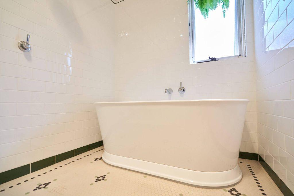 A modern bathroom showcasing a white bathtub and green tiles on the floor.