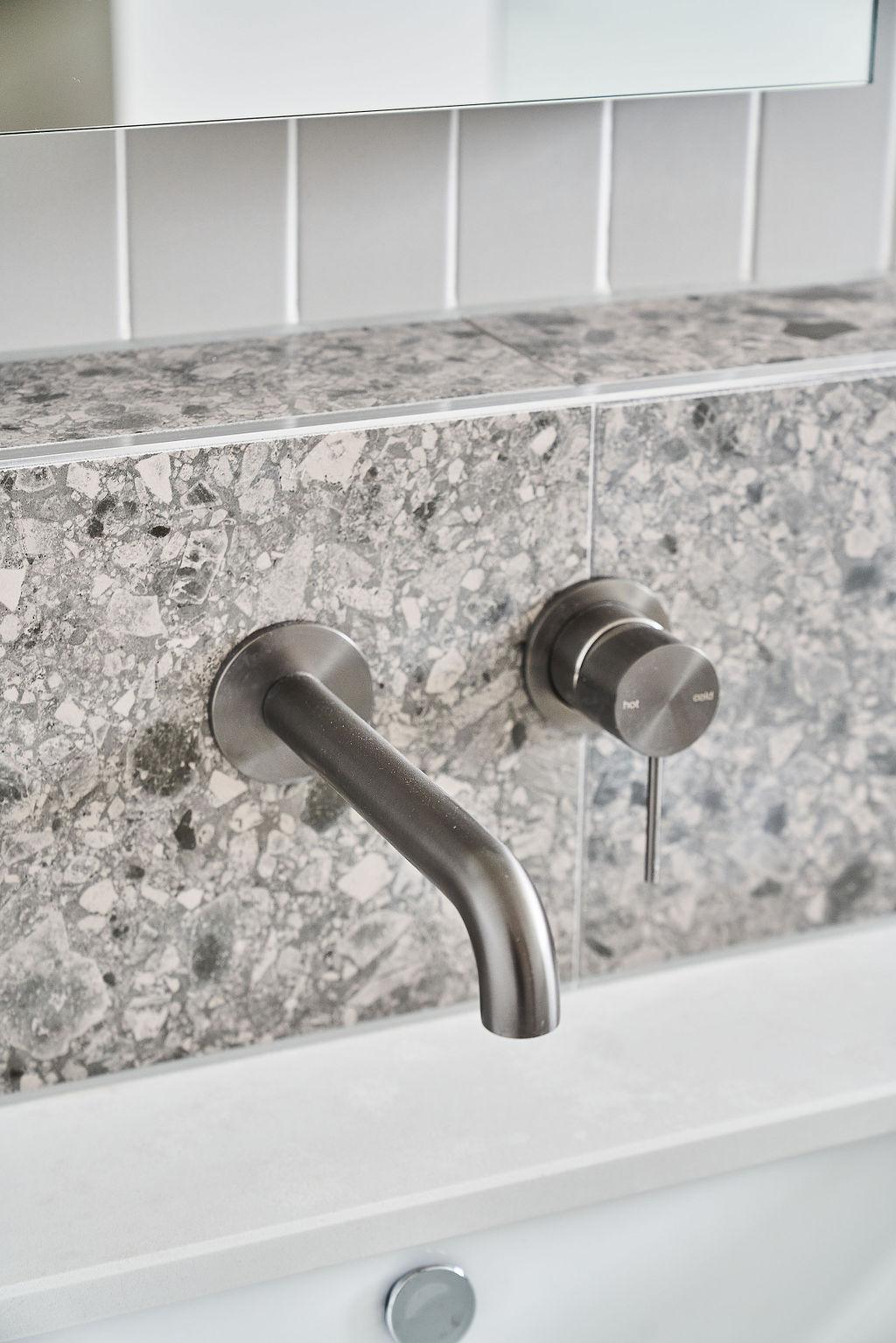 Wall-mounted gun metal tapware close-up against terrazzo tile splashback
