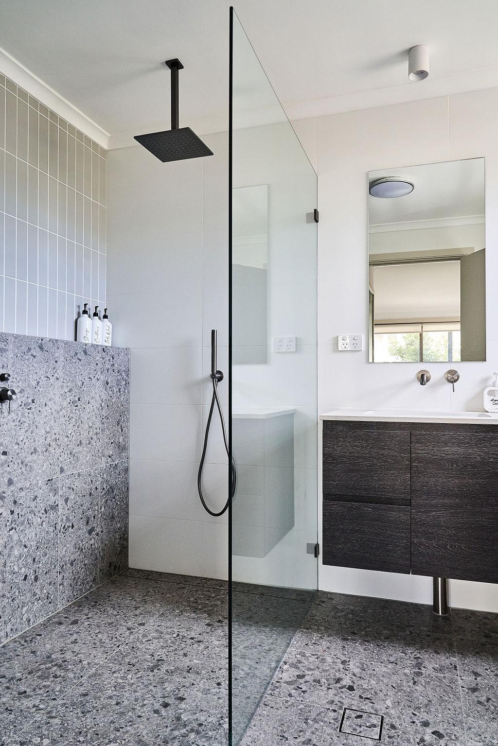 Shower recess with terrazzo tile wall, glass screen and dark timber vanity reflection