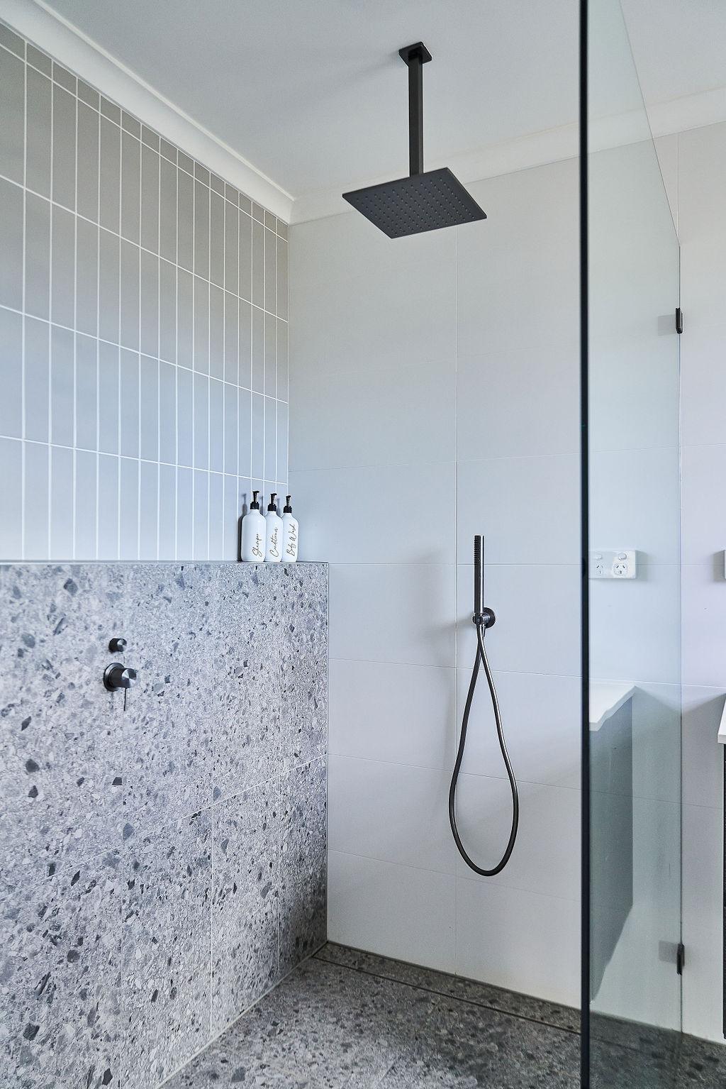 Ceiling shower head above terrazzo hob with styled bathroom amenity bottles
