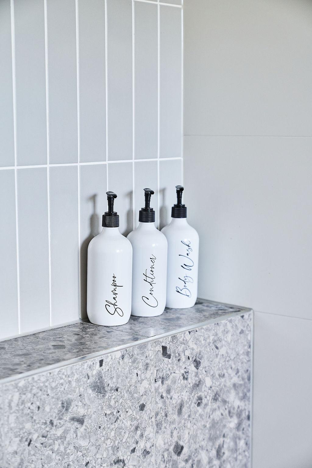 White panelled wall with styled amenity bottles on terrazzo shelf ledge