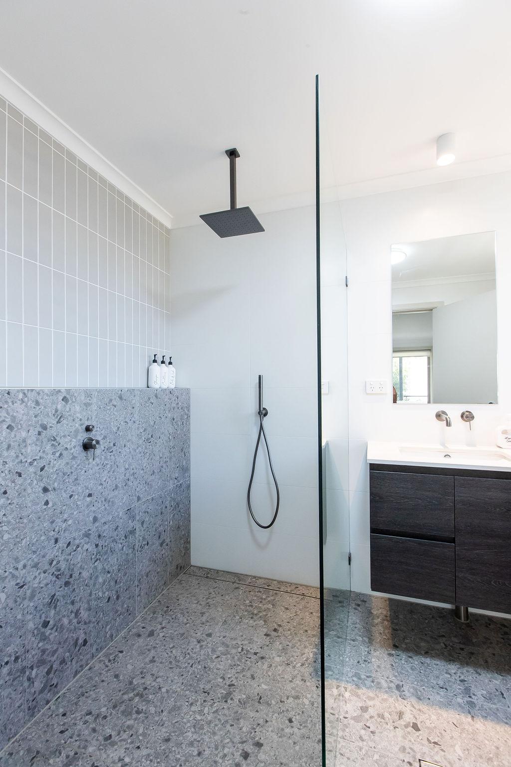 Ceiling-mounted shower head over terrazzo feature tile wall with glass screen