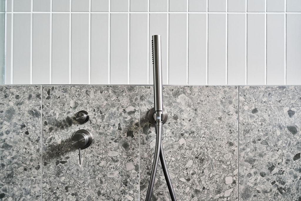 Close-up of gun metal handheld shower head against terrazzo tile wall