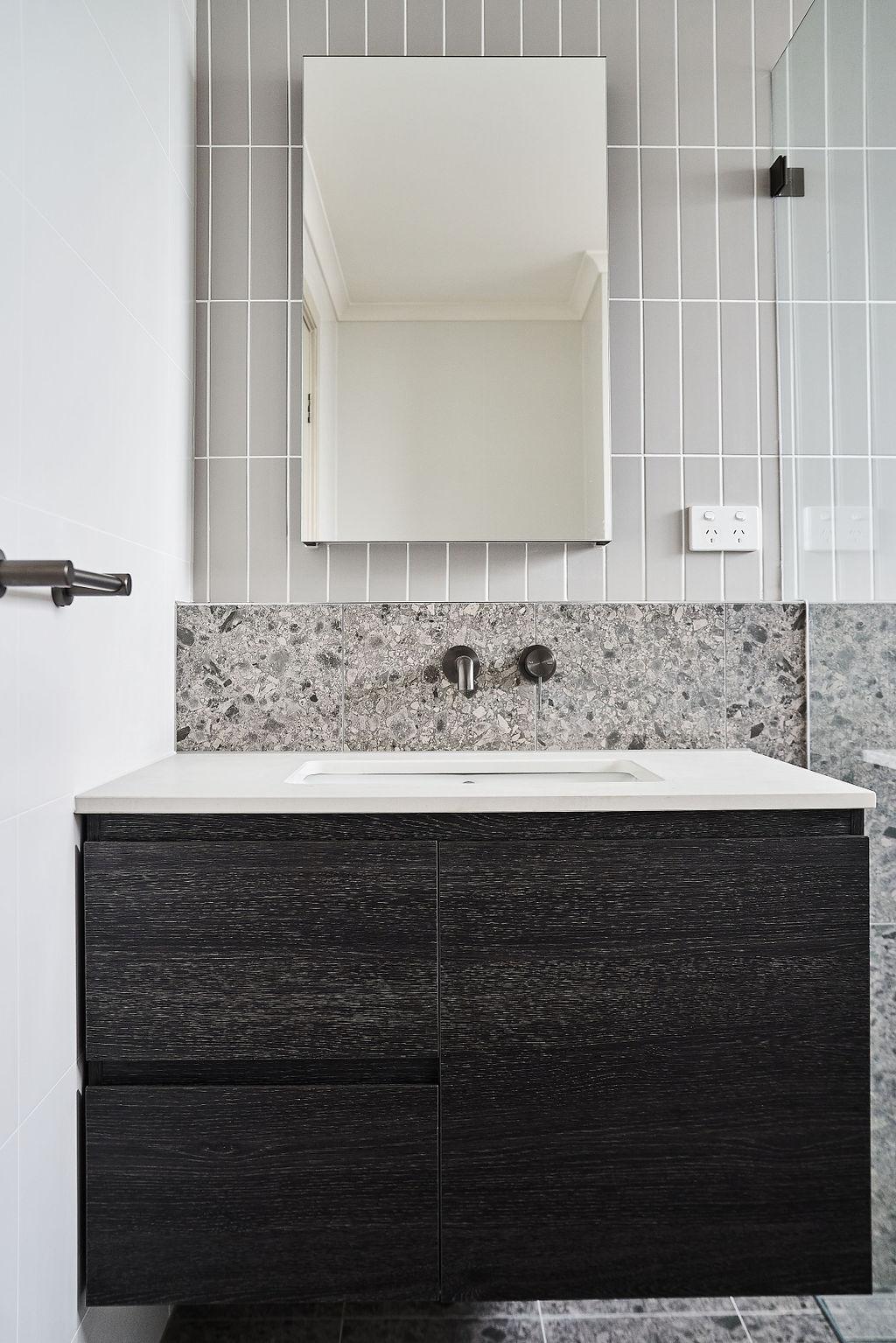 Mirror above vanity with terrazzo splashback, dark cabinet and wall-mounted tapware