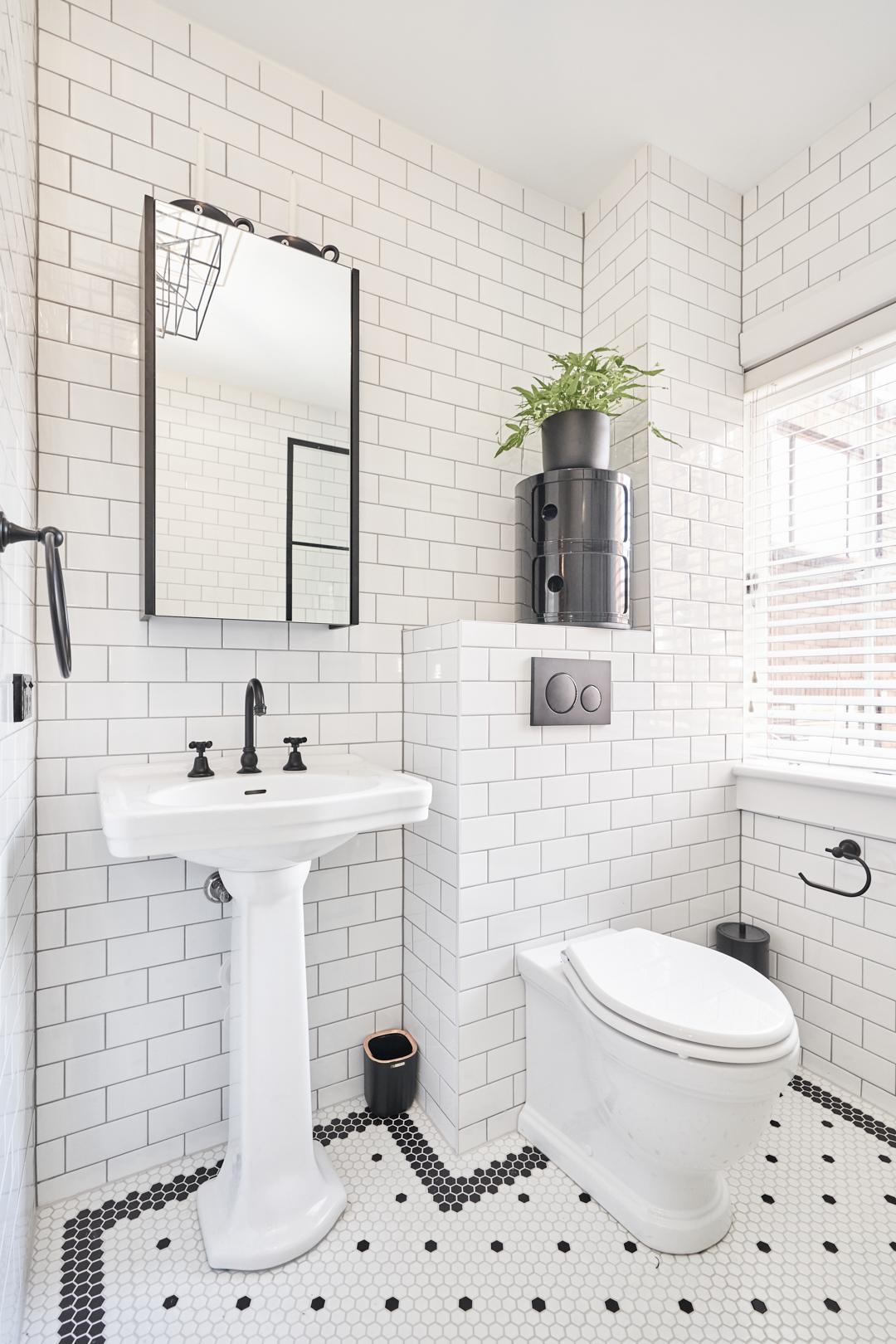 A sleek bathroom showcasing white wall tiles and a contrasting black and white tiled floor design.