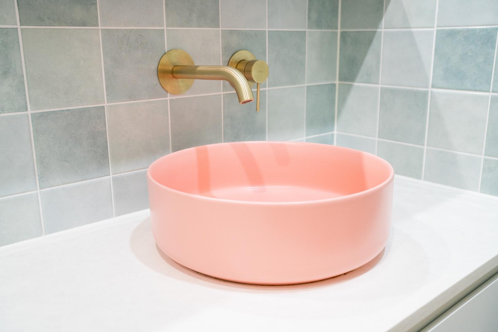 A bathroom interior with a pink sink bowl and a luxurious gold faucet.