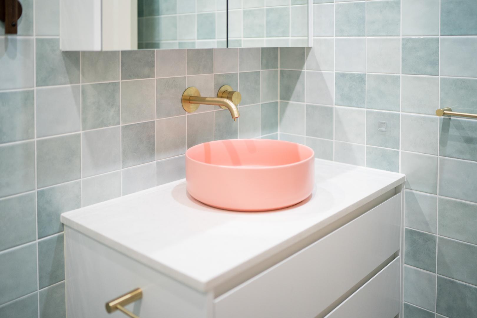 A bathroom interior with a pink sink bowl and a luxurious gold faucet.