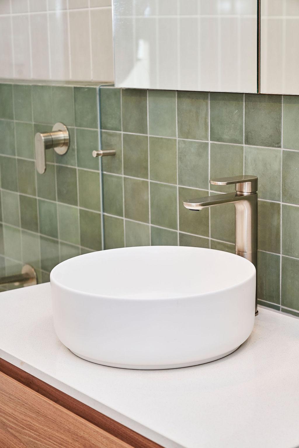A bathroom scene showcasing a white sink against a backdrop of green tiles, emphasizing a stylish design.