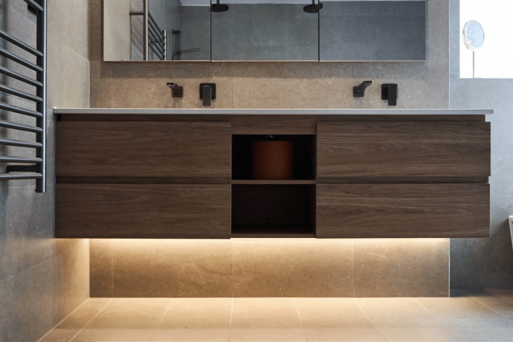 A modern bathroom featuring a wooden vanity and a stylish lighted mirror above it.