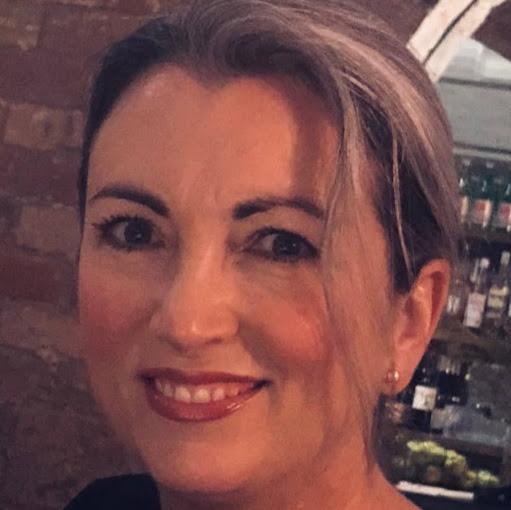 A woman with grey hair dressed in a black top, happily sharing her review of Origin Bathrooms & Kitchens.