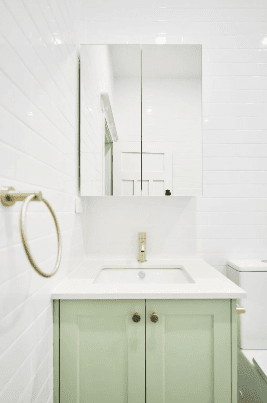 A bathroom featuring a green cabinet and white tiled walls and floor, creating a fresh and modern aesthetic.