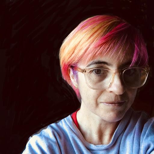 A woman with pink hair and glasses smiles while reviewing Origin Bathrooms & Kitchens.
