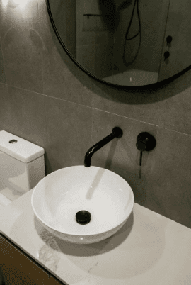 A clean bathroom with a white sink, toilet, and a large mirror above the sink, set against light-colored walls.