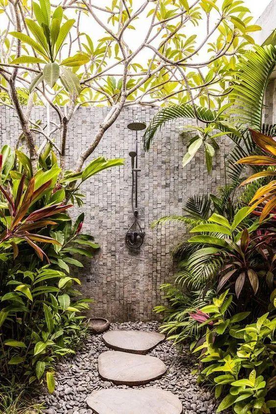 A garden walkway featuring a shower and lush plants on either side, creating a serene outdoor atmosphere.
