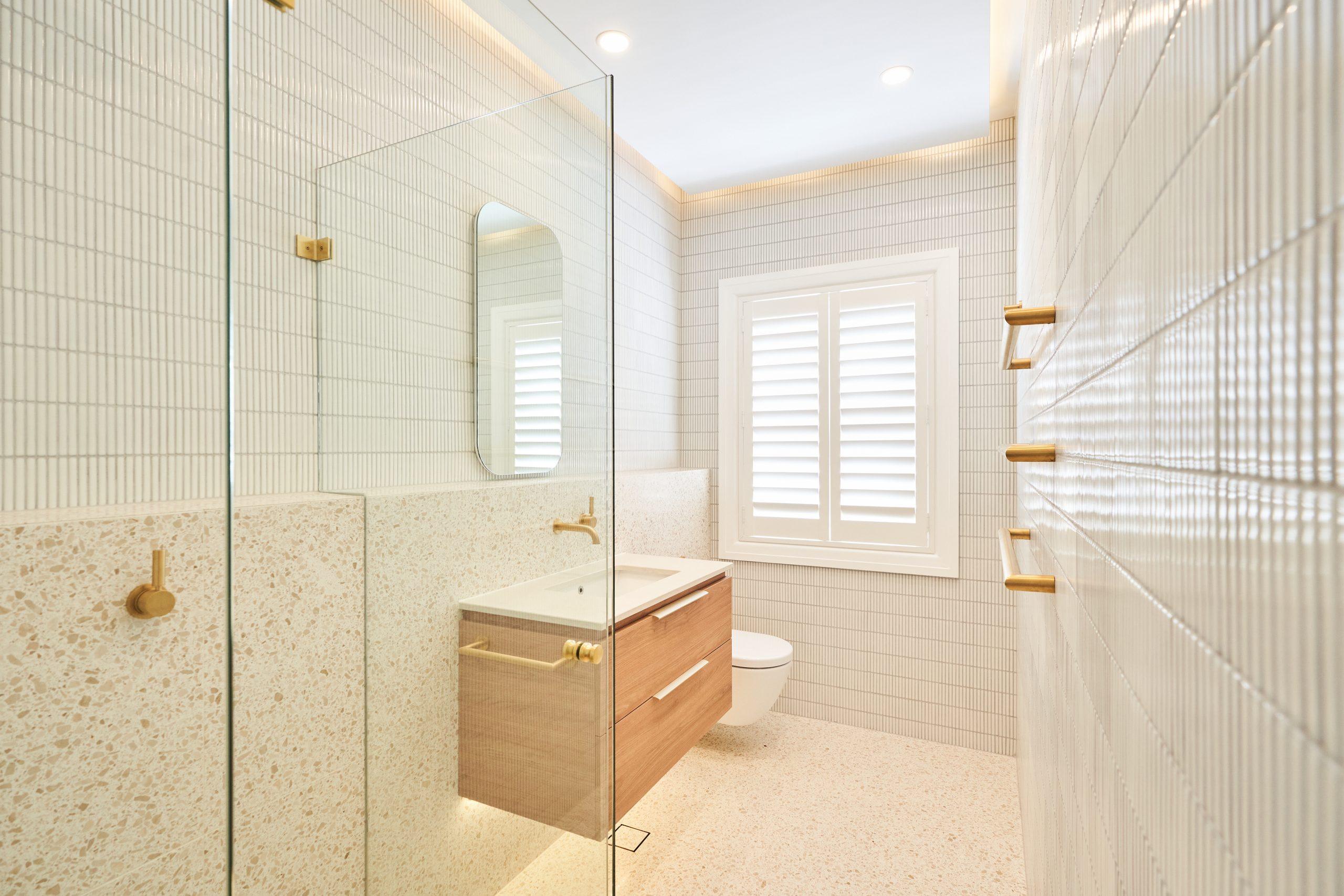 Stylish small Sydney bathroom with terrazzo floor, vertical wall tiles, wall-hung vanity, and brass fixtures.