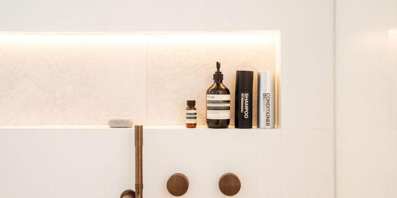 Modern Origin Bathrooms shower niche with shampoo, conditioner, Aesop products, and brass fixtures.
