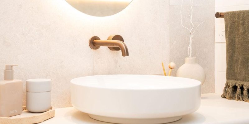 Elegant bathroom vanity with round countertop basin, brushed brass tapware, and minimalist decor.