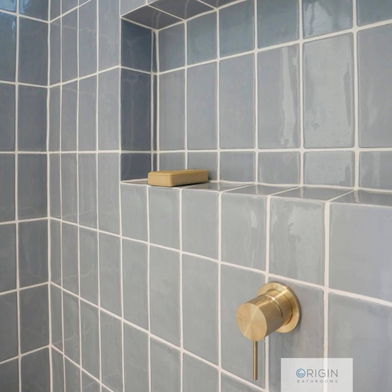 A blue tiled shower featuring a sleek brass faucet, showcasing a modern and stylish bathroom design.